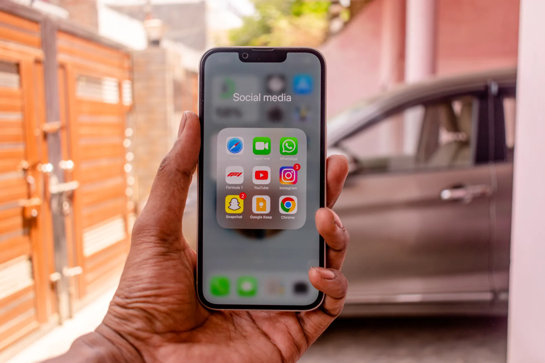 Buyer holding a phone with app folders open, a used car parked in the background