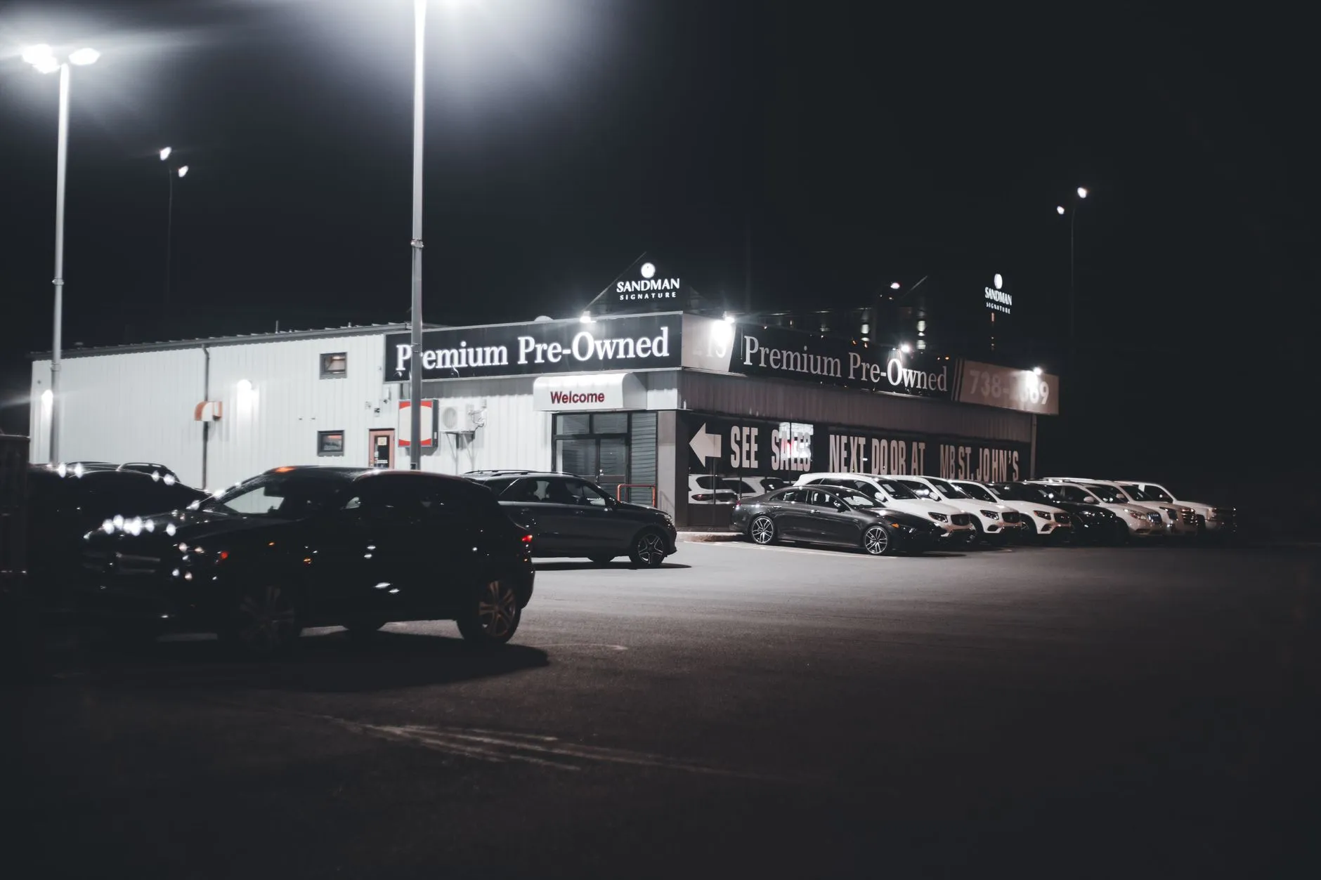 Used cars lined up on a dealership lot at night, the kind of common economy vehicles a beginner should flip first