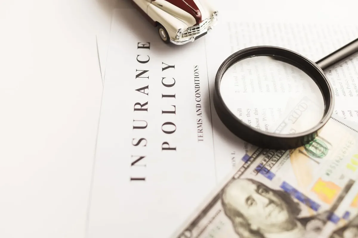Car insurance policy on a desk with a toy car, a magnifying glass and cash