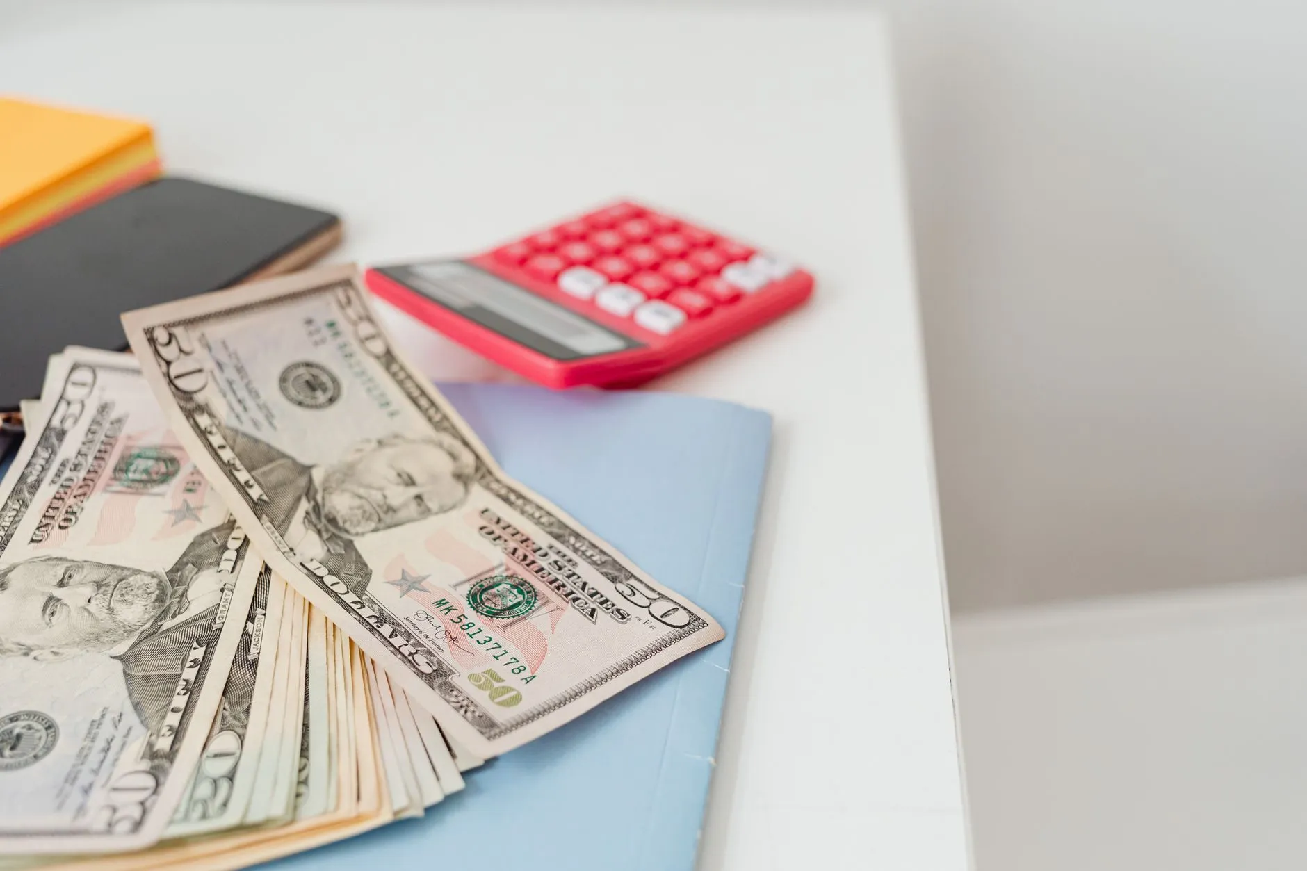 Calculator, US dollars, and notebooks on a desk for working out used car flip profit